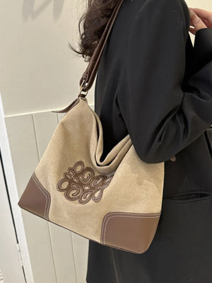 Ochre suede hobo bag with brown appliqué and contrast stitching, worn with a black blazer.