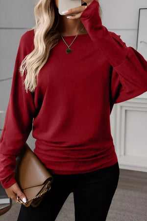 Burgundy long-sleeve blouse with ruched waist and crew neck, styled with black pants and a brown clutch.