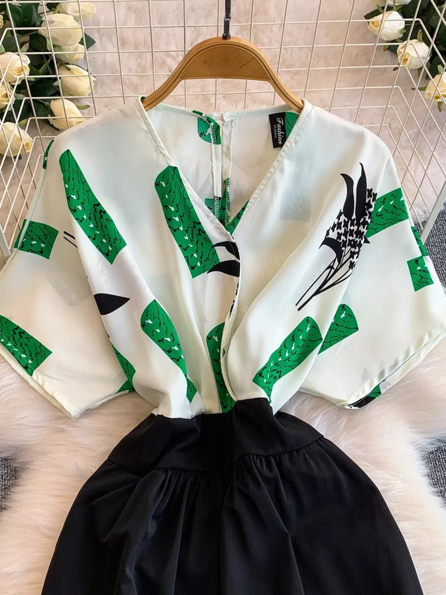White romper with green abstract print, V-neck, short sleeves, and black wide-leg pants.