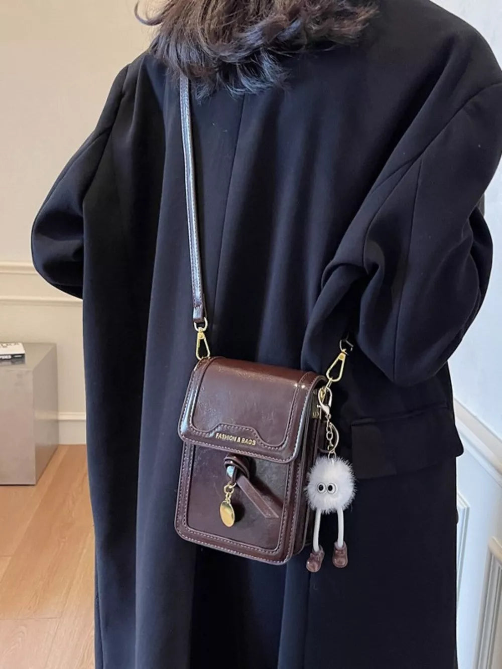 Caramel mini pu leather crossbody bag with charm, worn with black coat.