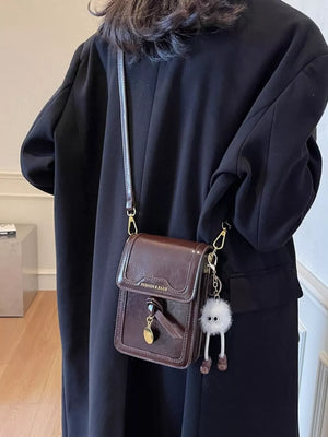 Caramel mini pu leather crossbody bag with charm, worn with black coat.