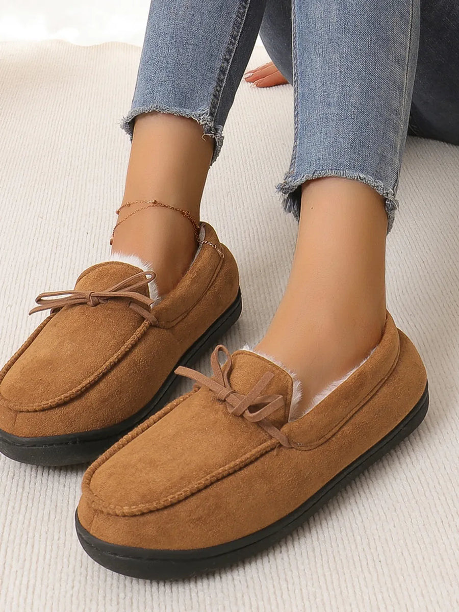 Caramel suede moccasin slippers with faux fur lining and bow detail.
