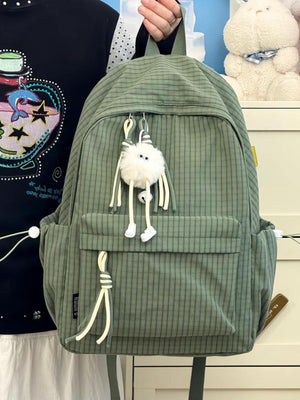 Green plaid nylon backpack with fuzzy charm and tassel details.