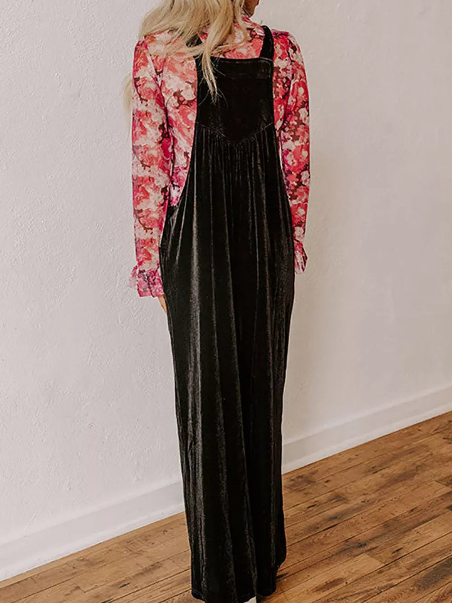 Black velvet wide-leg romper with adjustable straps and a V-neck bodice, worn over a floral print top.