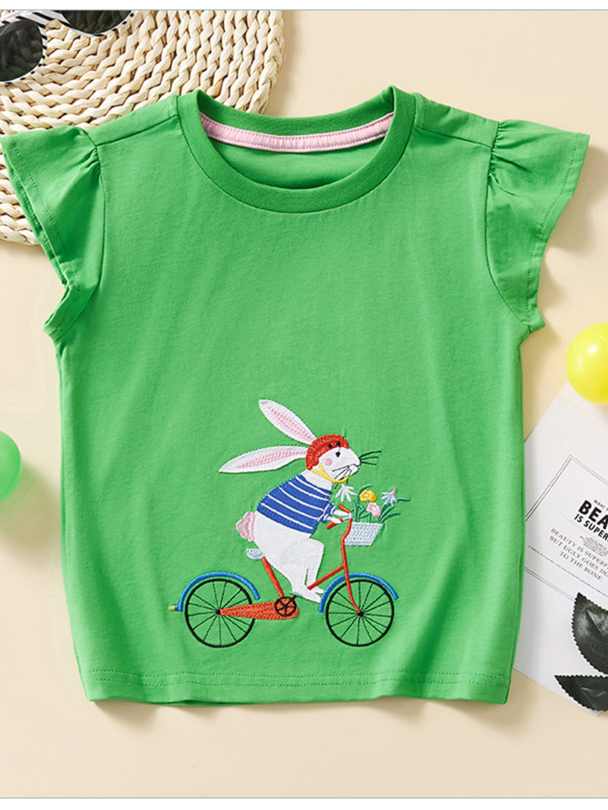 Green cotton cap sleeve t-shirt with embroidered rabbit on a bicycle.