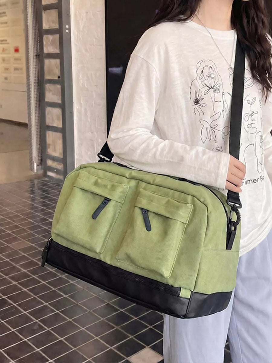 Green duffle bag with two front zip pockets and black trim, worn crossbody.