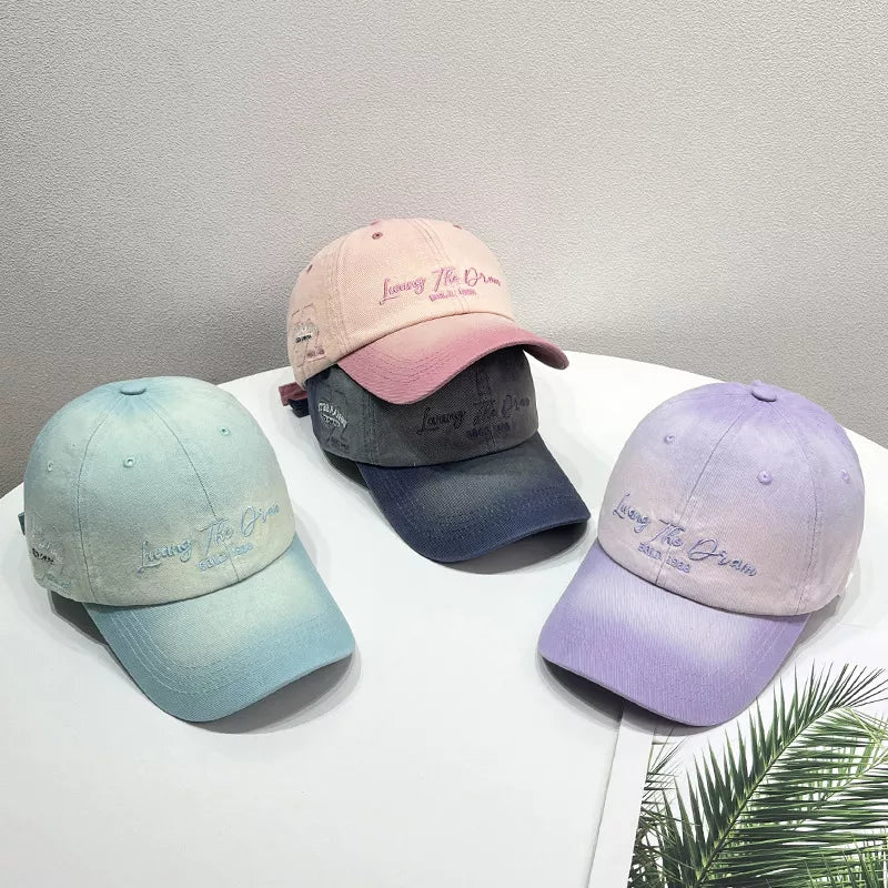 Gradient embroidered cotton baseball caps in light purple, dark blue, and peach powder colors.