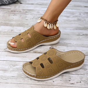 Camel laser-cut comfort slide sandals with decorative stitching and a seashell anklet.