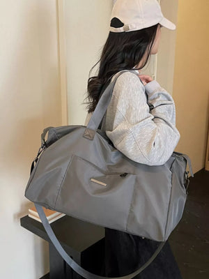 Minimalist large grey Oxford cloth travel bag with front pockets and a crossbody strap.