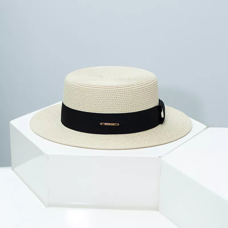 Woven straw boater hat in beige with black ribbon band and gold accent.