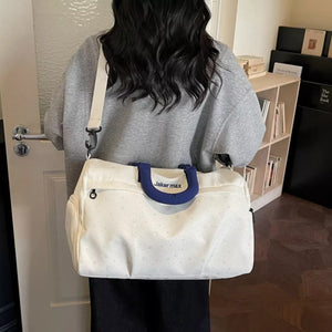 Cream white duffel bag with crescent moon and star pattern, blue handles, and adjustable strap.