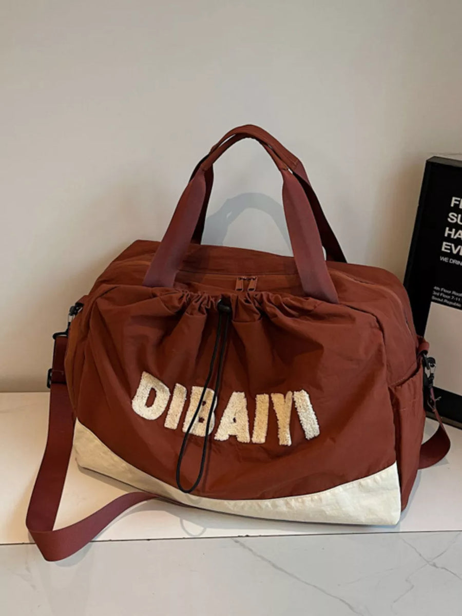 Chic color-blocked travel bag with adjustable strap and embroidered logo detail.