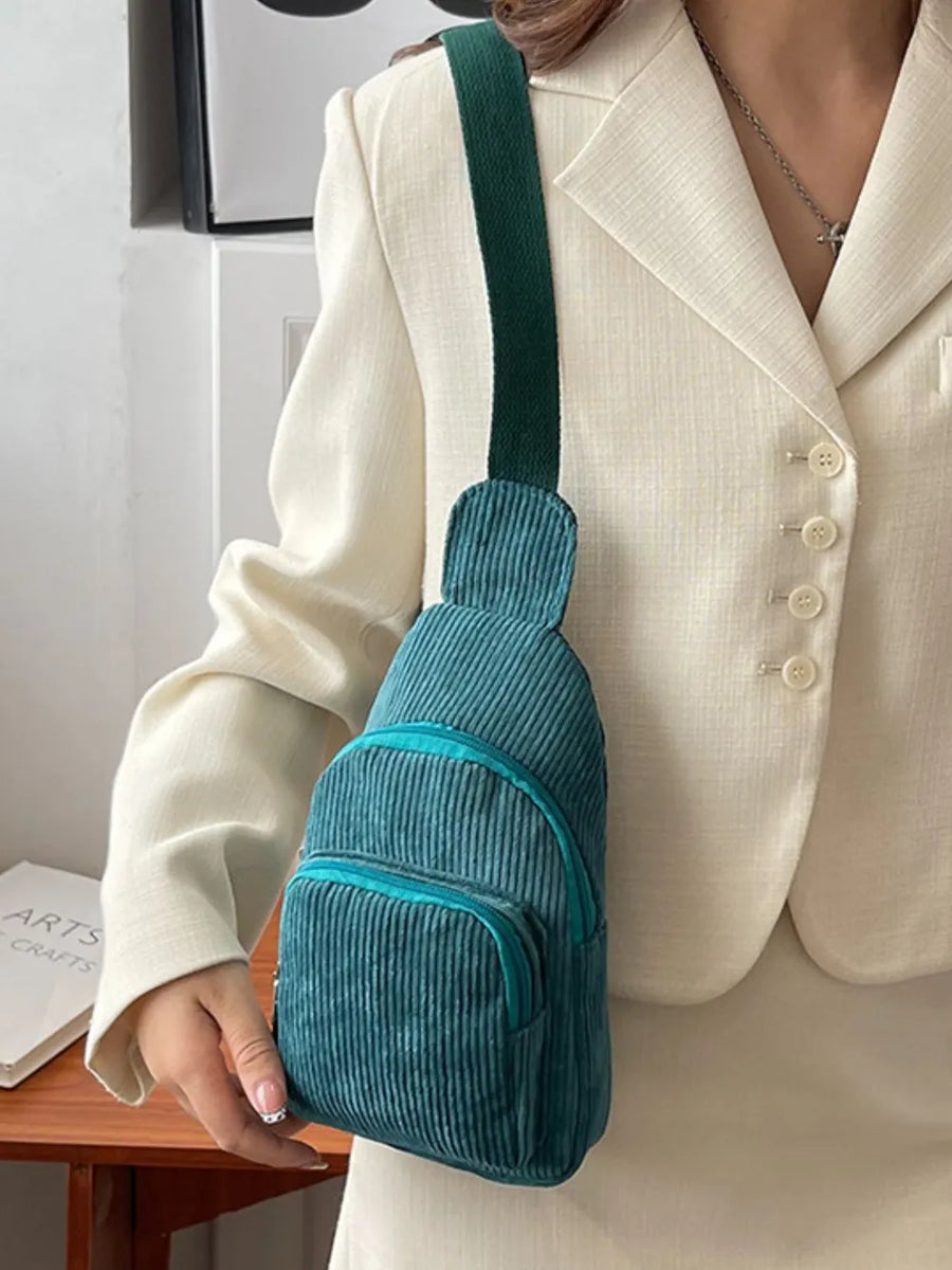 Deep Teal corduroy sling bag with zip pockets and green strap, worn casually.