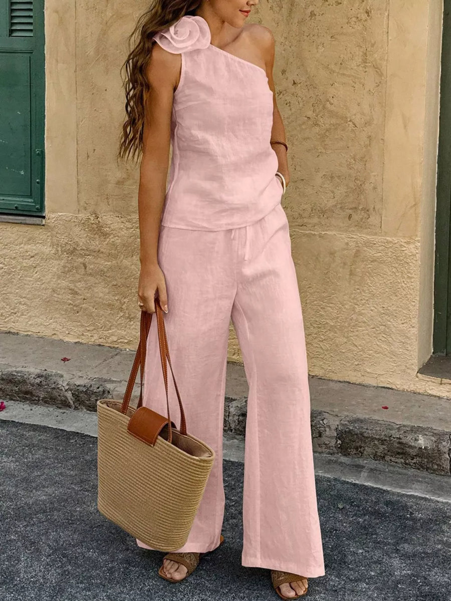 Pink cotton one-shoulder top with floral embellishment and wide-leg pants.