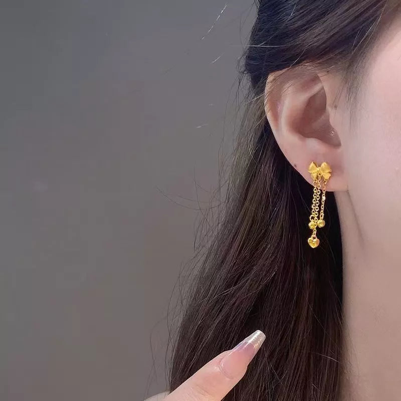 Gold bowknot tassel earrings with heart charms and delicate chains.