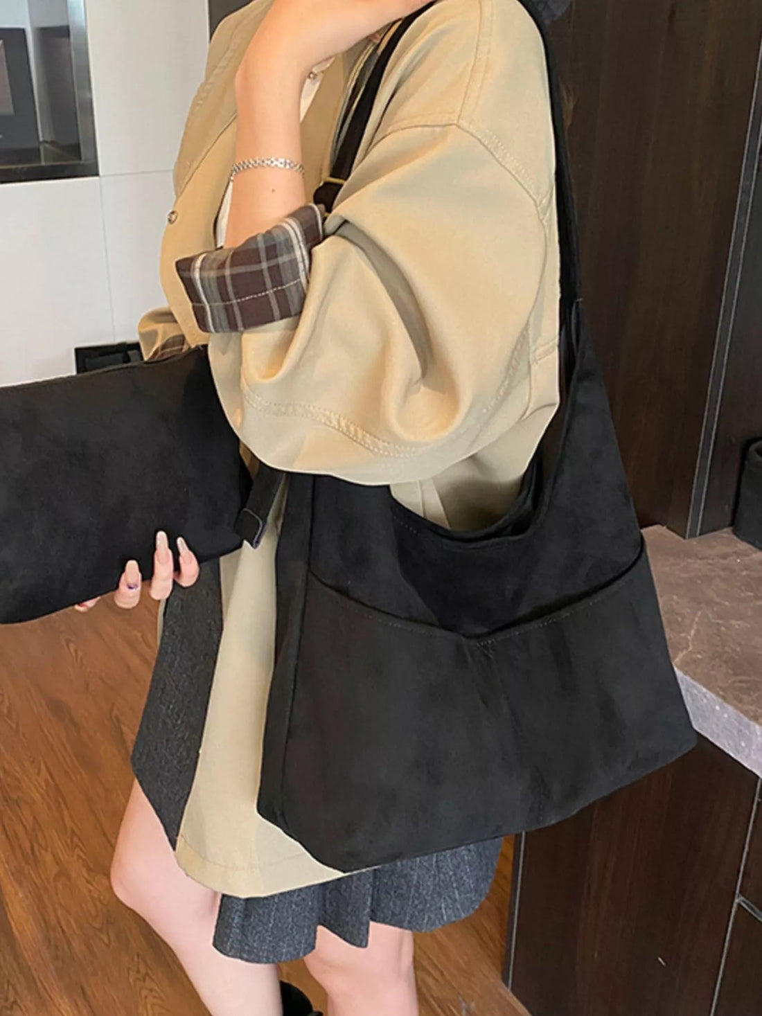 Large black suede shoulder bag with front pockets and adjustable strap.