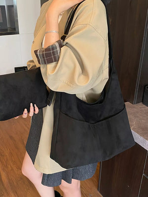 Large black suede shoulder bag with front pockets and adjustable strap.