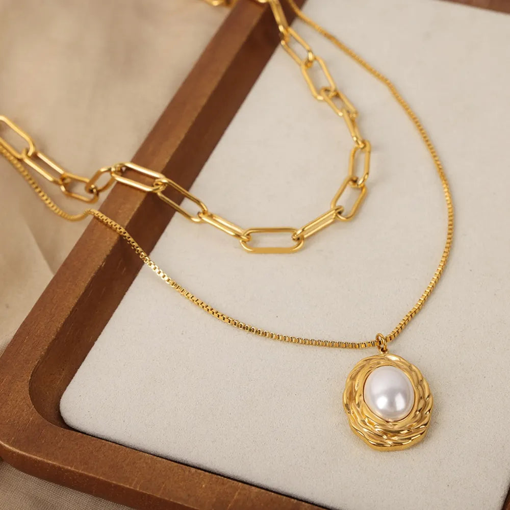 Gold double-layered necklace with paperclip chain and oval pearl pendant.