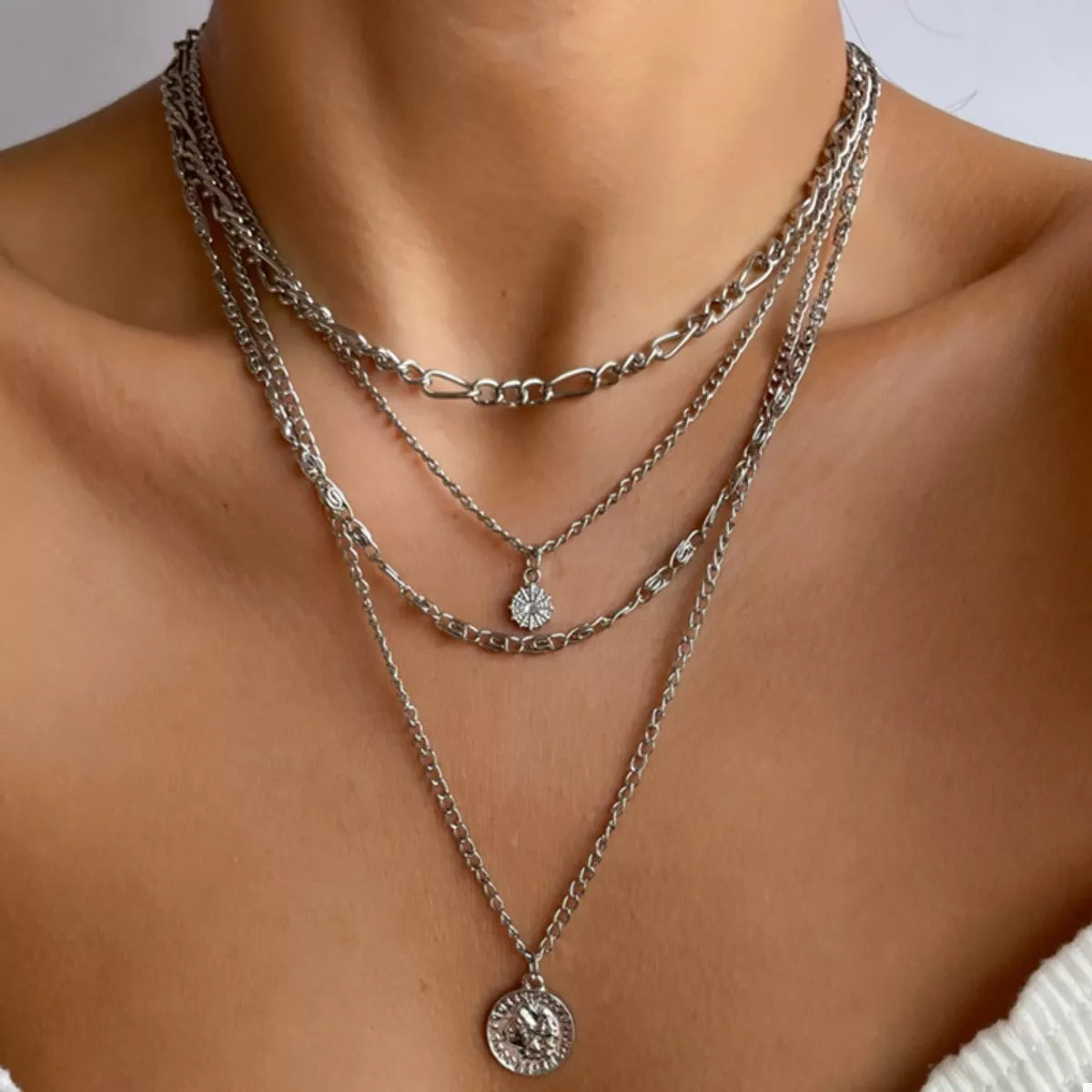 Layered silver coin pendant necklace with a small starburst charm.
