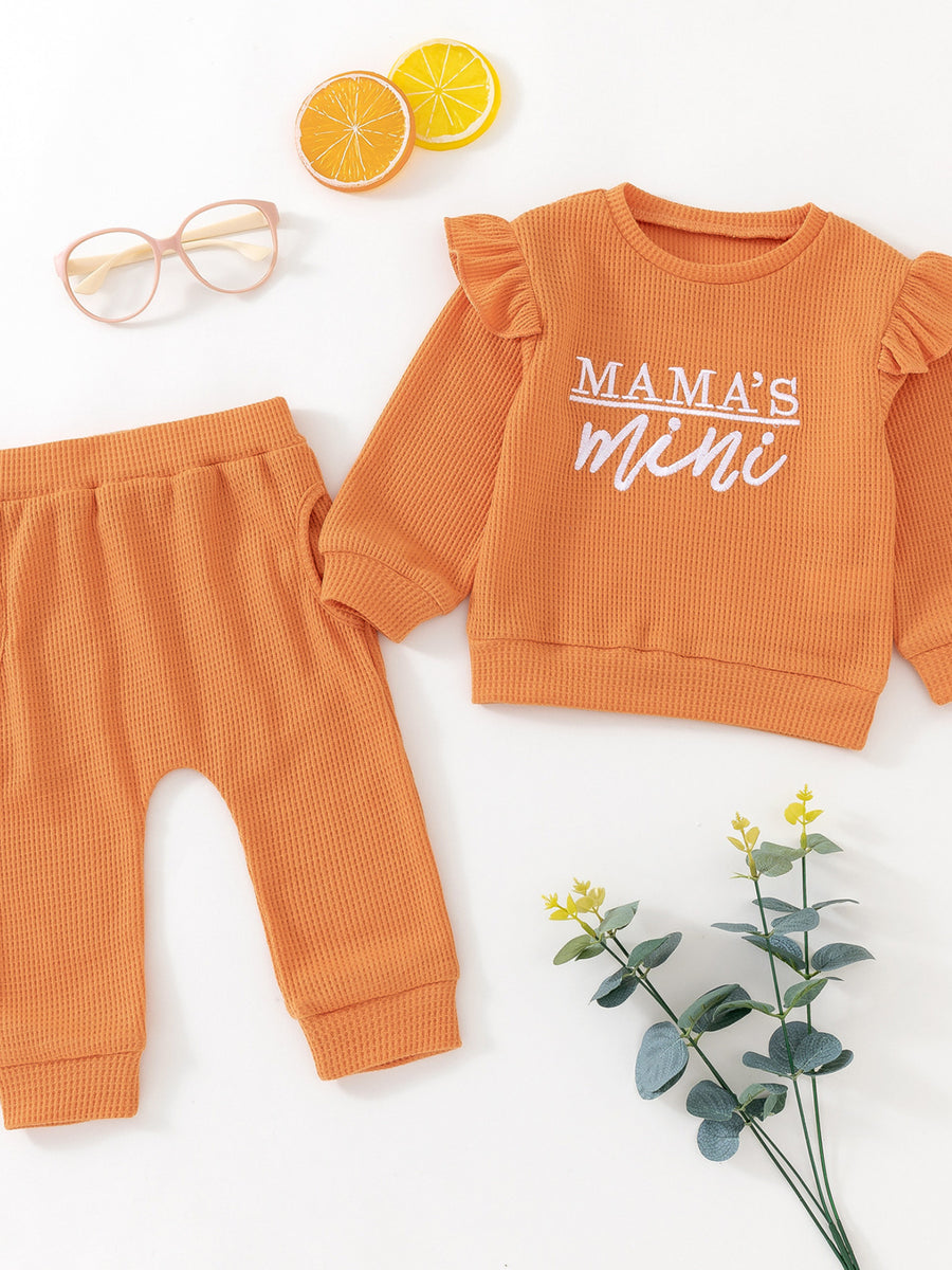 Orange waffle knit toddler top with ruffled sleeves and "Mama's Mini" graphic, paired with matching pants.