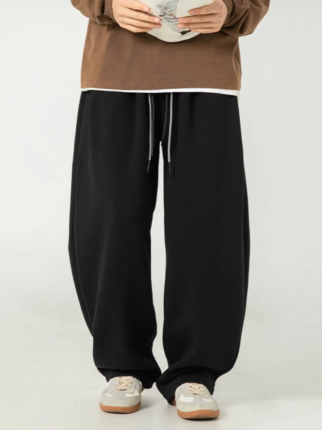 Black oversized lounge trousers with drawstring and wide leg, styled with sneakers.