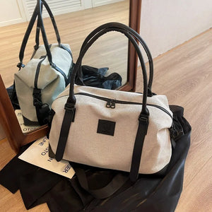Canvas weekend holdall duffel bag in light beige with black leather handles and trim.