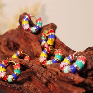 Rainbow enamel segmented hoop earrings with gold accents, displayed on wood.