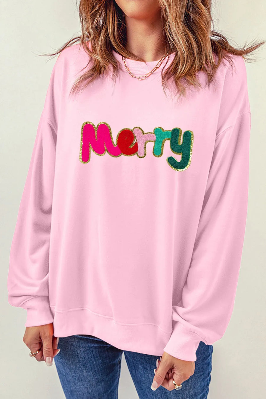 Blush pink crewneck sweatshirt with embroidered colorful "Merry" text and gold trim.