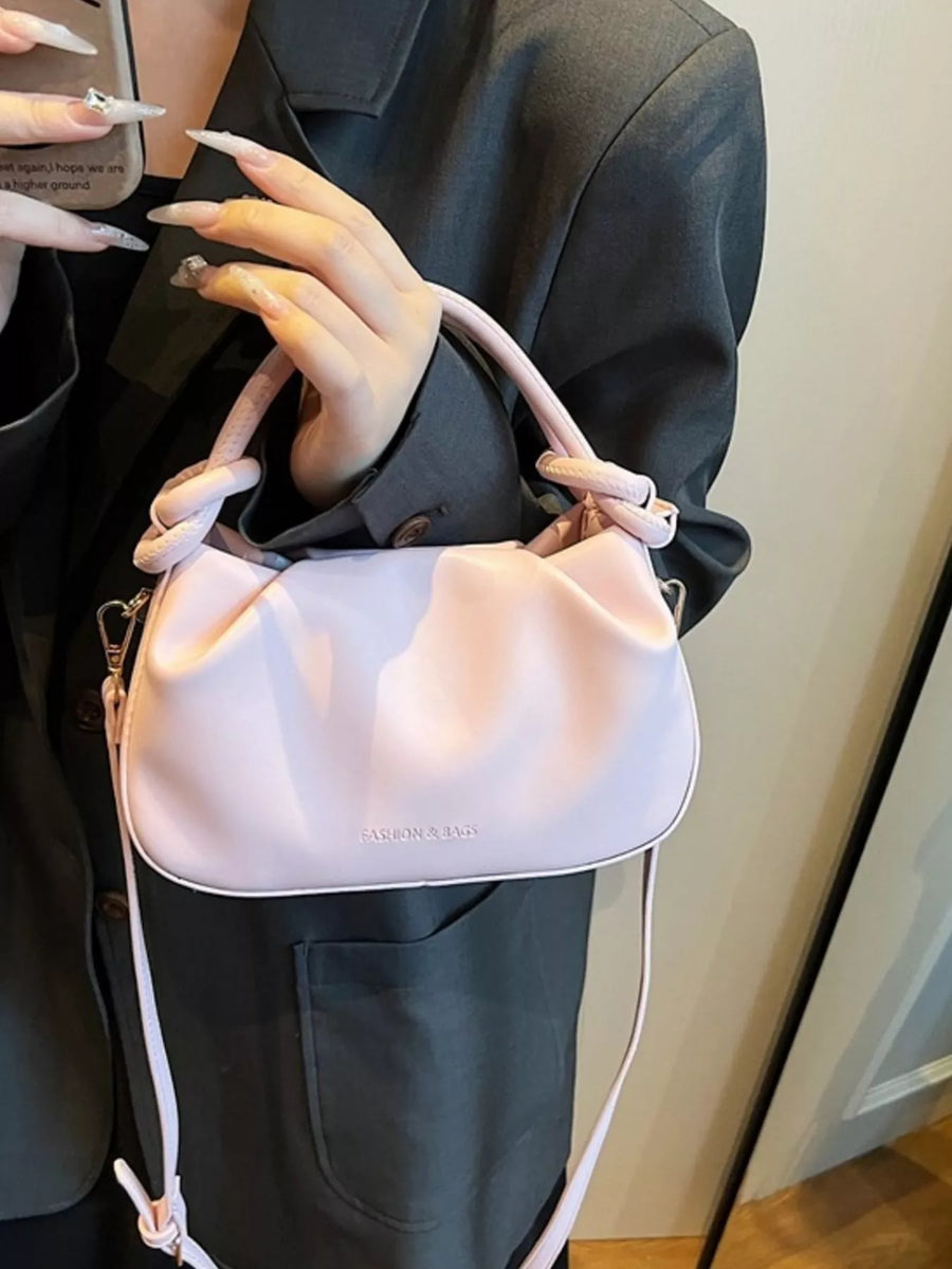 Pink ruched crossbody bag with knotted top handles and a long strap.