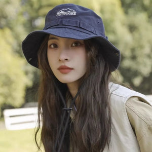 Navy bucket hat with embroidered mountain logo and chin strap, worn by a woman.