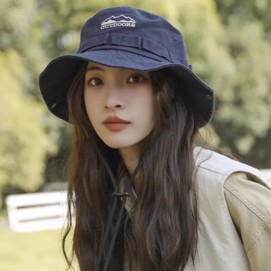 Navy bucket hat with embroidered mountain logo and chin strap, worn by a woman.