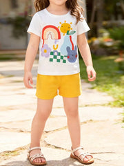 White cotton graphic tee with rainbow, sun, bunny, and fruit print, paired with yellow shorts.