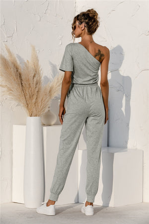 Gray asymmetric sweat jumpsuit with drawstring waist and cuffed jogger pants.
