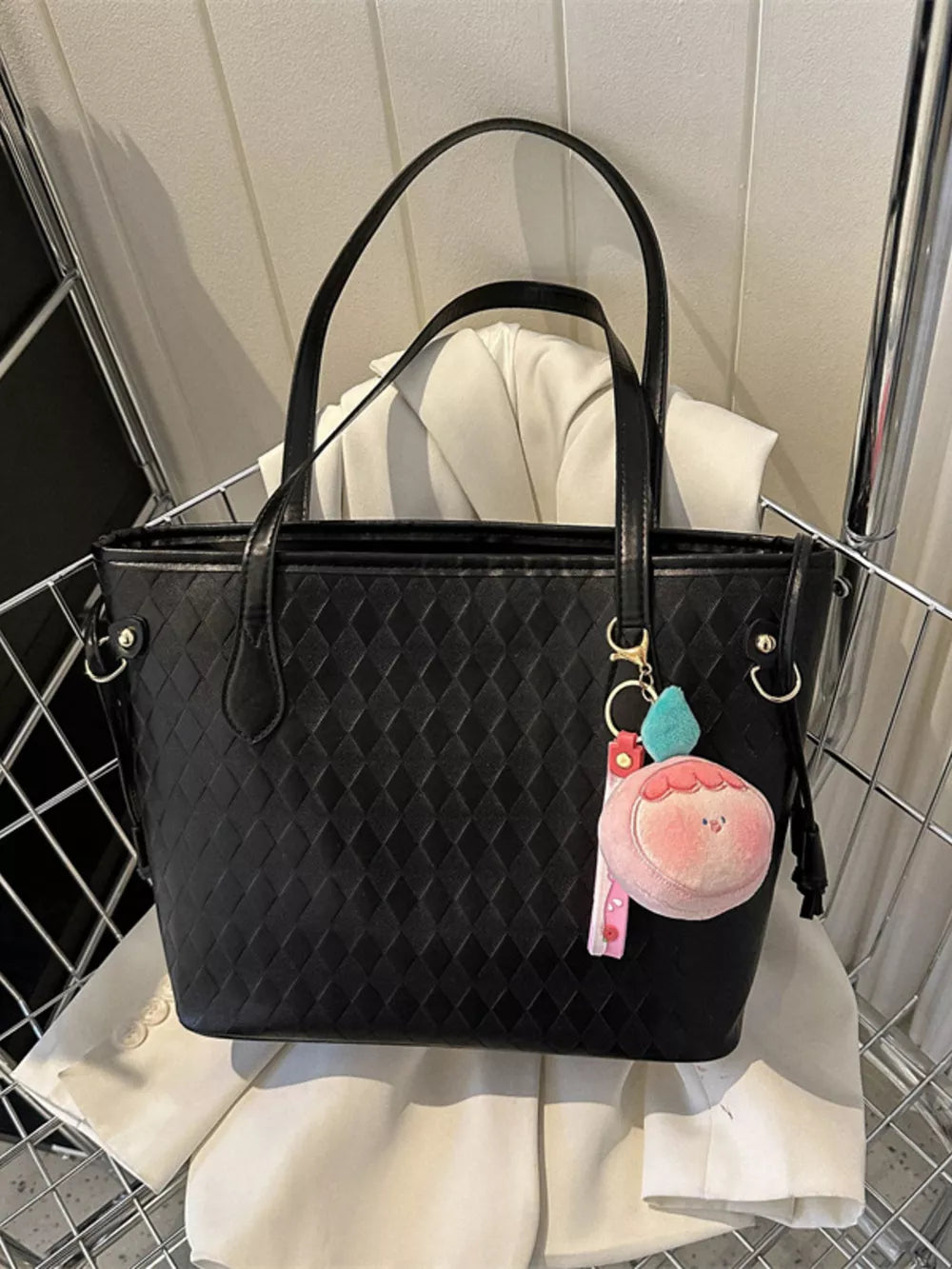Black textured diamond woven tote bag with a cute peach charm and pink strap detail.