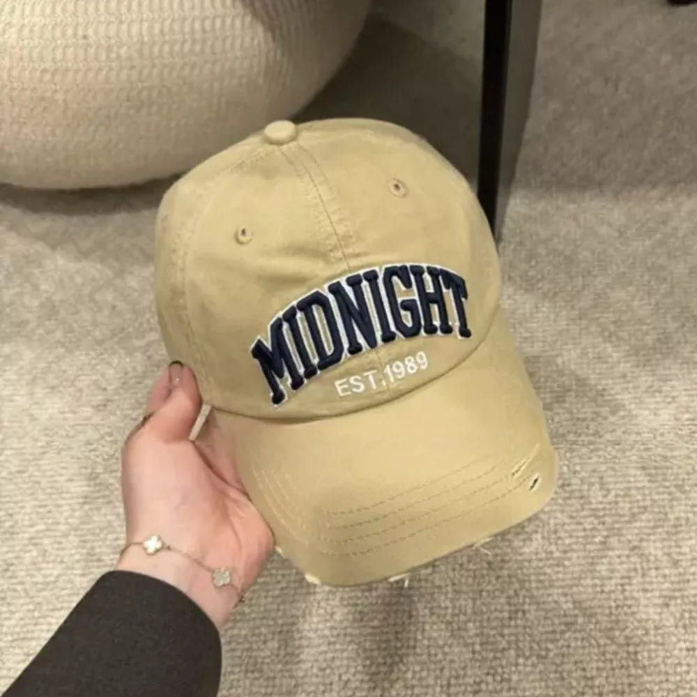 Distressed khaki baseball cap with navy blue "MIDNIGHT EST. 1989" embroidery.