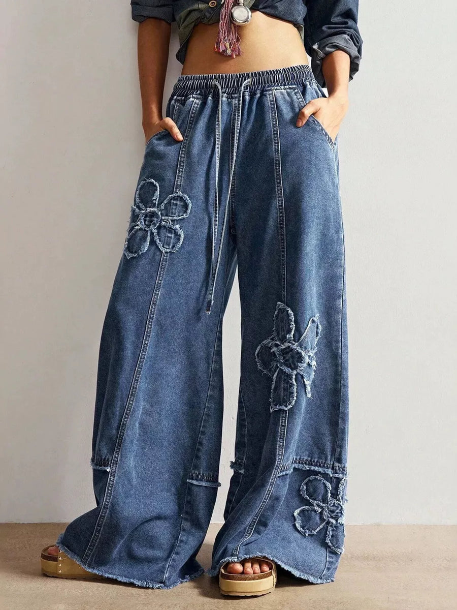 Wide leg denim jeans in blue with distressed floral appliques and drawstring waist.
