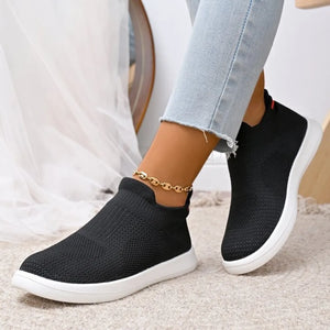 Black knit slip-on sneakers with white soles and a gold anklet.