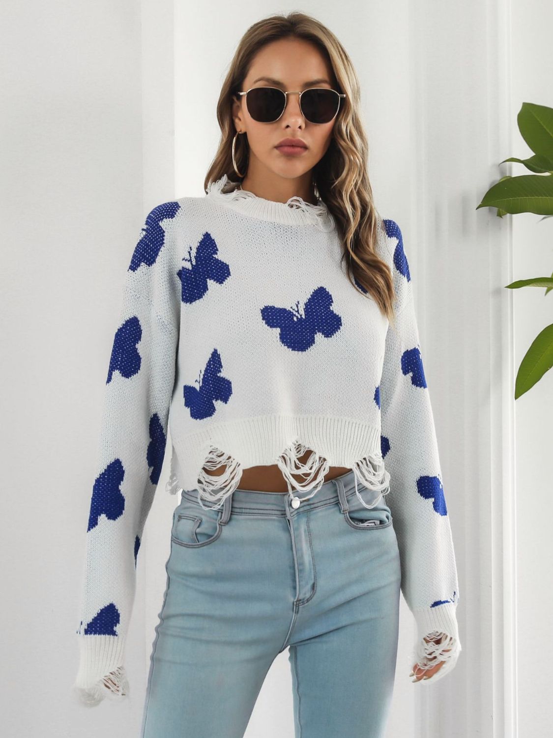 White cropped knit sweater with distressed details and a blue butterfly print.