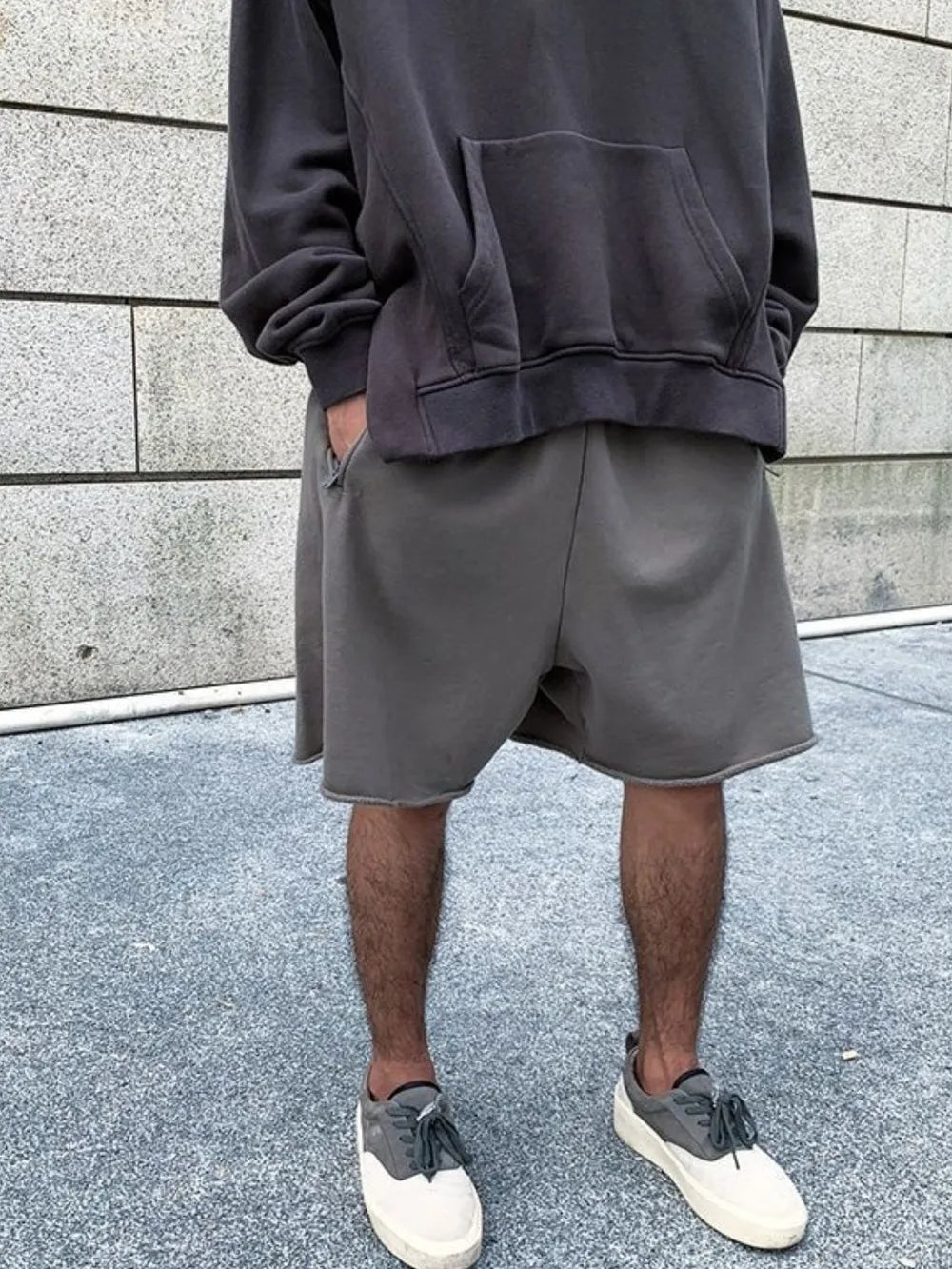 Gray relaxed fit shorts with raw hem, styled with a hoodie and sneakers.