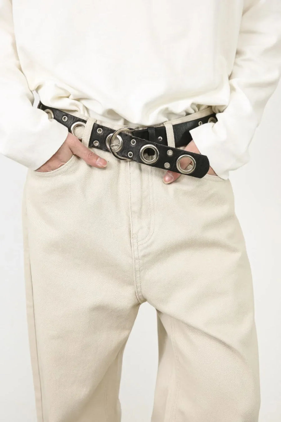 Oversized beige denim jeans with a black grommet belt and silver hardware.