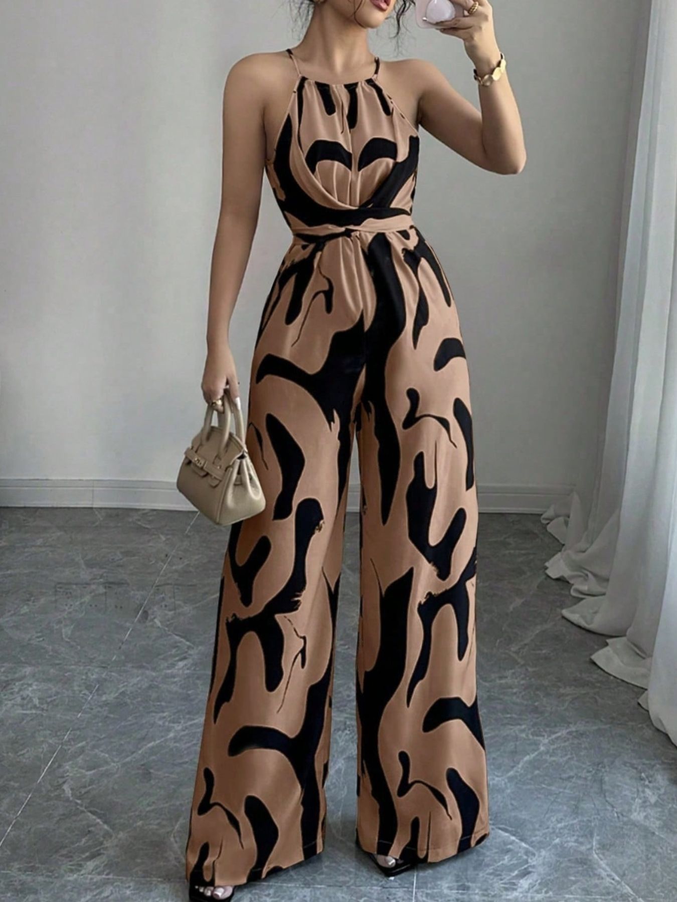 Elegant wide-leg jumpsuit in tan with abstract black print, halter neck, and draped bodice.