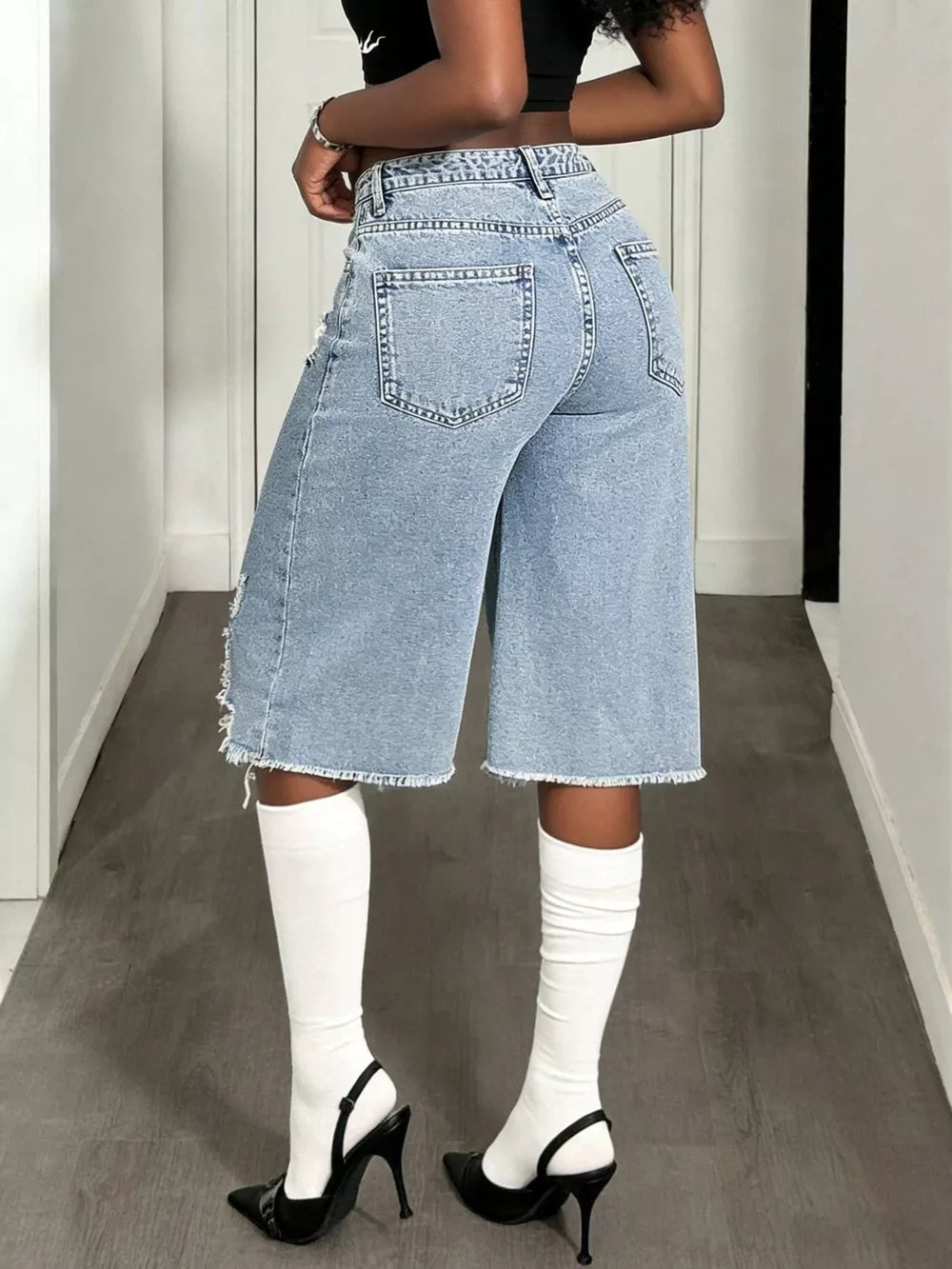 Distressed light wash denim wide-leg shorts with raw hem and distressed details.