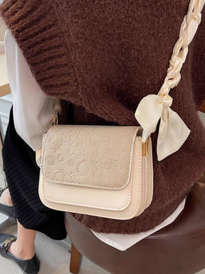 Mini two-tone crossbody bag in beige with embossed cartoon pattern and braided strap.
