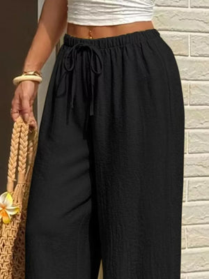 Black wide-leg linen pants with drawstring waist and textured fabric.