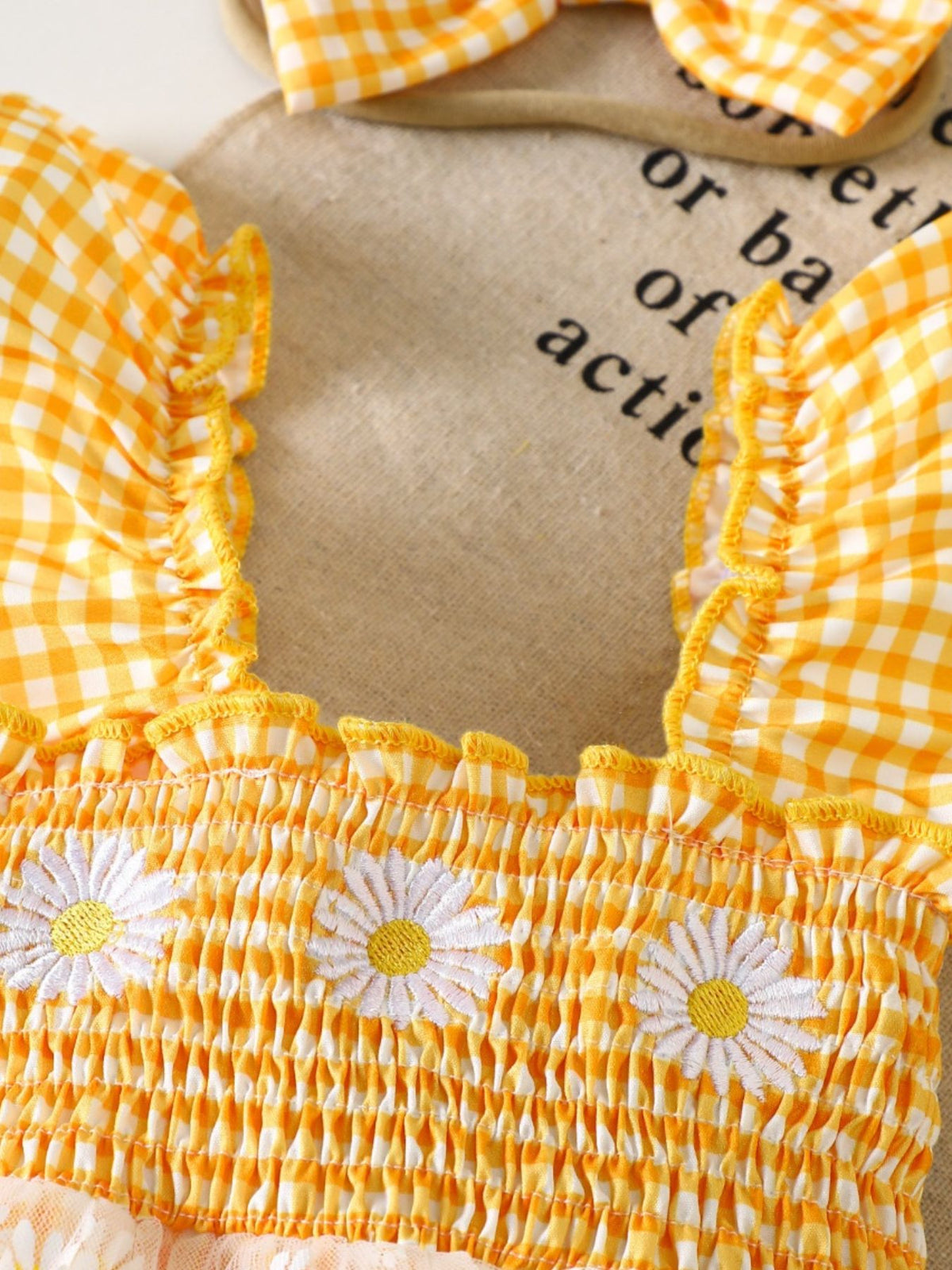 Yellow gingham baby one-piece with smocked bodice, daisy embroidery, and ruffle sleeves.