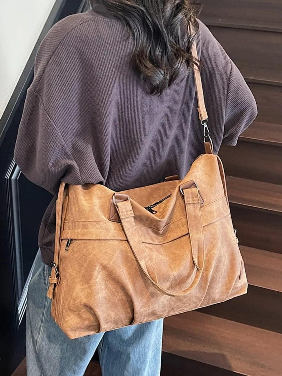 Brown faux leather tote bag with top handles and adjustable strap, worn with a brown waffle knit top.