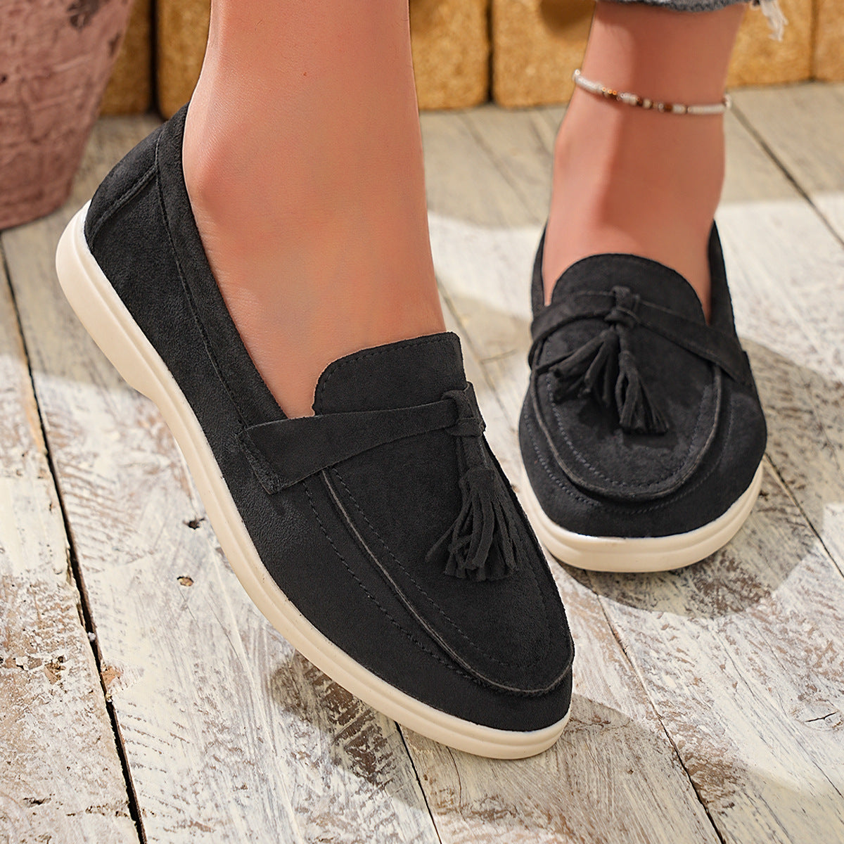 Black faux-suede slip-on loafers with decorative tassels and a flat sole.