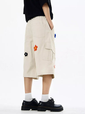 Tan cotton cargo shorts with floral appliqués and wide legs.