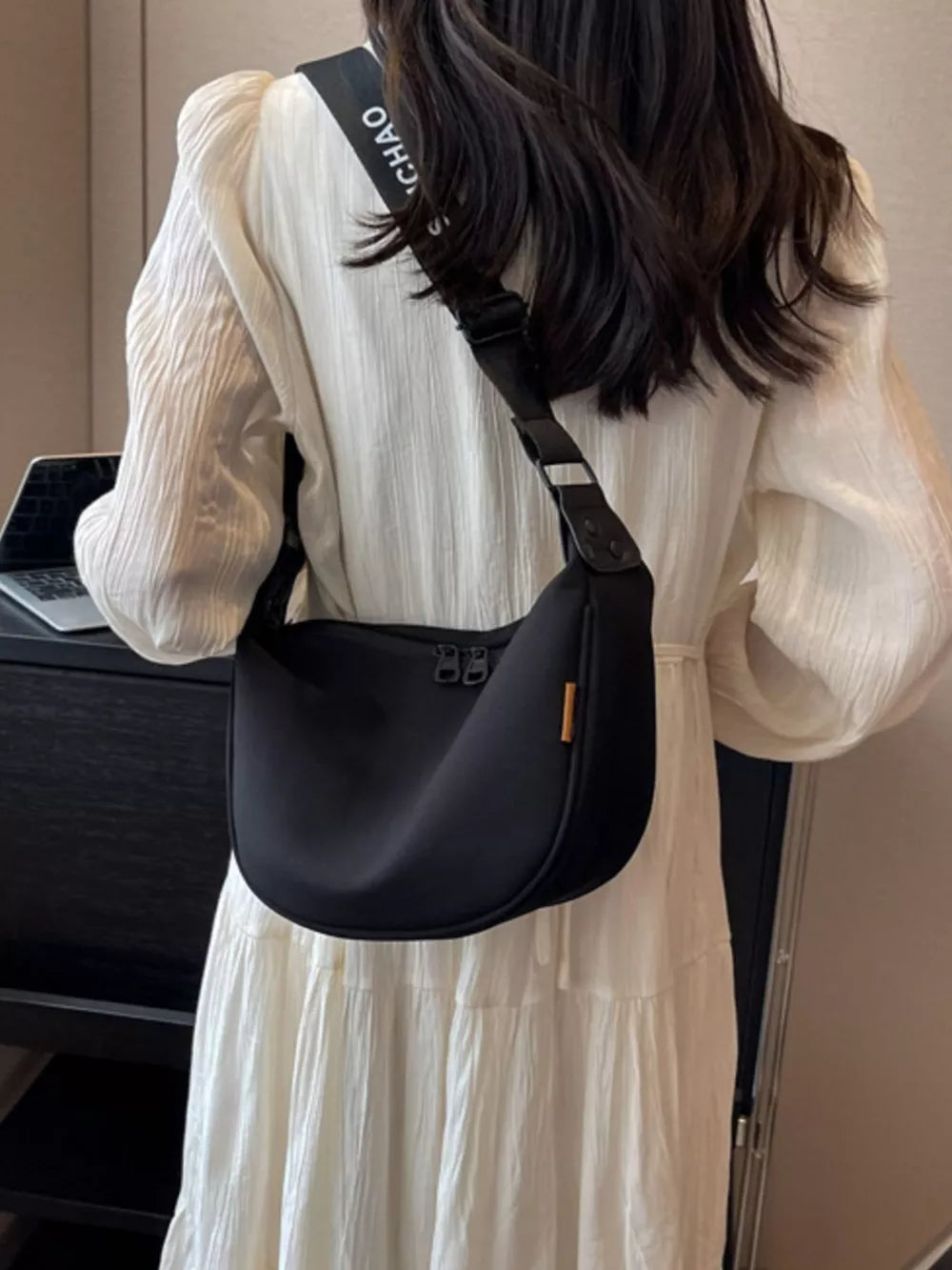 Black crescent-shaped crossbody bag with adjustable strap and double zipper closure.
