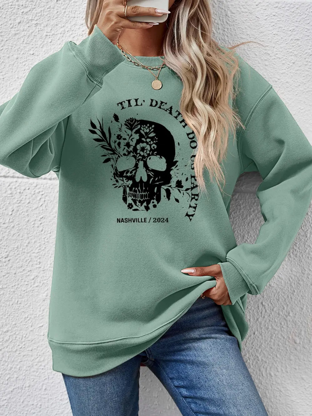 Sage green raglan sweatshirt with floral skull graphic and text